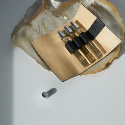 Stylish perfume sample bottles in a leather case on a seashell, showcasing elegance on a white surface.